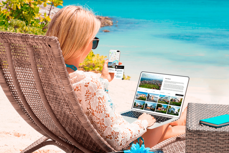 a wealthy woman sitting on a chair in front of the beach searching for million dollar properties on a real estate website with her laptop. She looks comfortable holding a phone chatting with a realtor helping her with property information